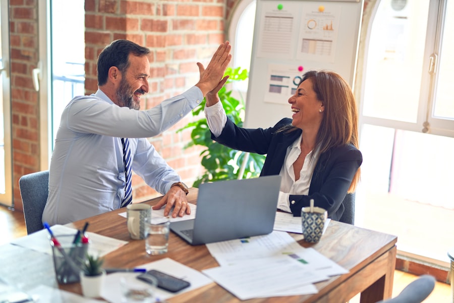 Two business professionals high-fiving over a laptop, representing a successful client partnership